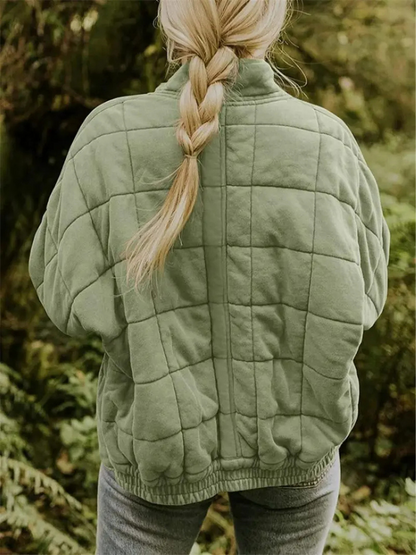 Frau mit geflochtenem Haar trägt grüne Steppjacke im Wald. Outdoor-Mode, Herbstkleidung, Natur, Freizeitkleidung.