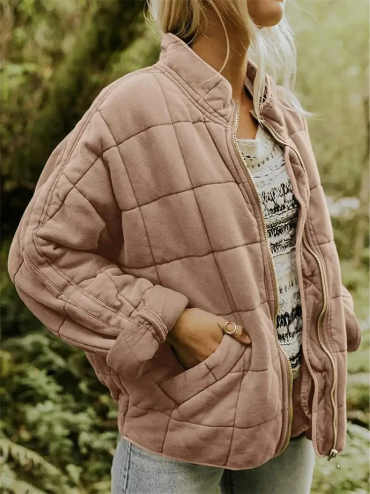 Frau in rosa Steppjacke, lässig über gestreiftem Pullover und Jeans, im Freien. Modetrend Herbst, warme Damenbekleidung, Outdoor-Stil.