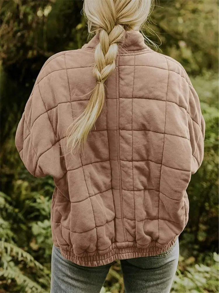 Blonde Frau mit geflochtenem Zopf trägt eine gesteppte, beige Jacke im Wald. Outdoor-Mode, Herbstkleidung, Natur, Freizeitlook.