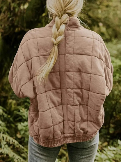 Blonde Frau mit geflochtenem Zopf trägt eine gesteppte, beige Jacke im Wald. Outdoor-Mode, Herbstkleidung, Natur, Freizeitlook.