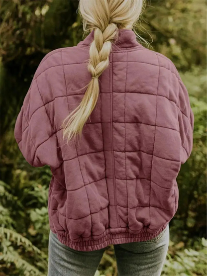 Frau mit geflochtenem Haar trägt eine gesteppte, lila Jacke im Freien. Herbstmode, Outdoor-Bekleidung, gemütlicher Stil.