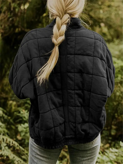 Blonde Frau mit geflochtenem Zopf trägt schwarze gesteppte Jacke im Wald. Outdoor-Mode, Herbstkleidung, Naturhintergrund.