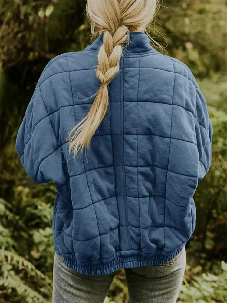 Frau mit blauer Steppjacke und geflochtenem Haar im Wald. Outdoor-Mode, Herbstkleidung, Natur, Freizeitjacke, Damenbekleidung.