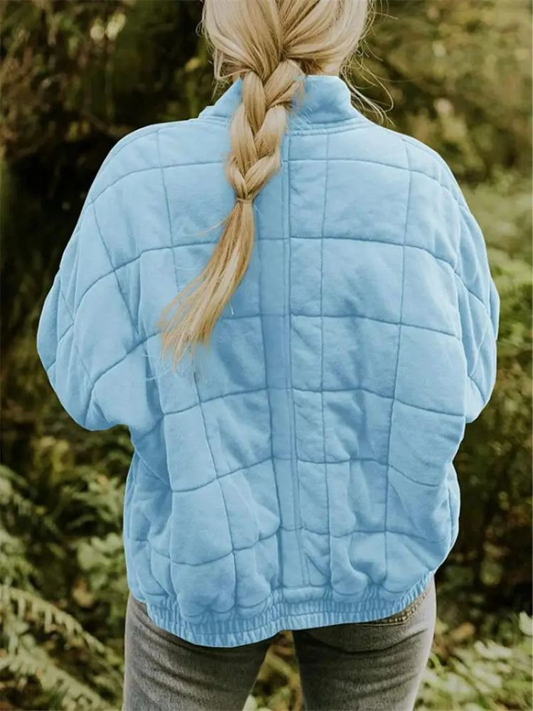 Blonde Frau mit geflochtenem Zopf trägt eine blaue Steppjacke im Freien. Natur, Herbstmode, Outdoor-Bekleidung, Rückansicht.