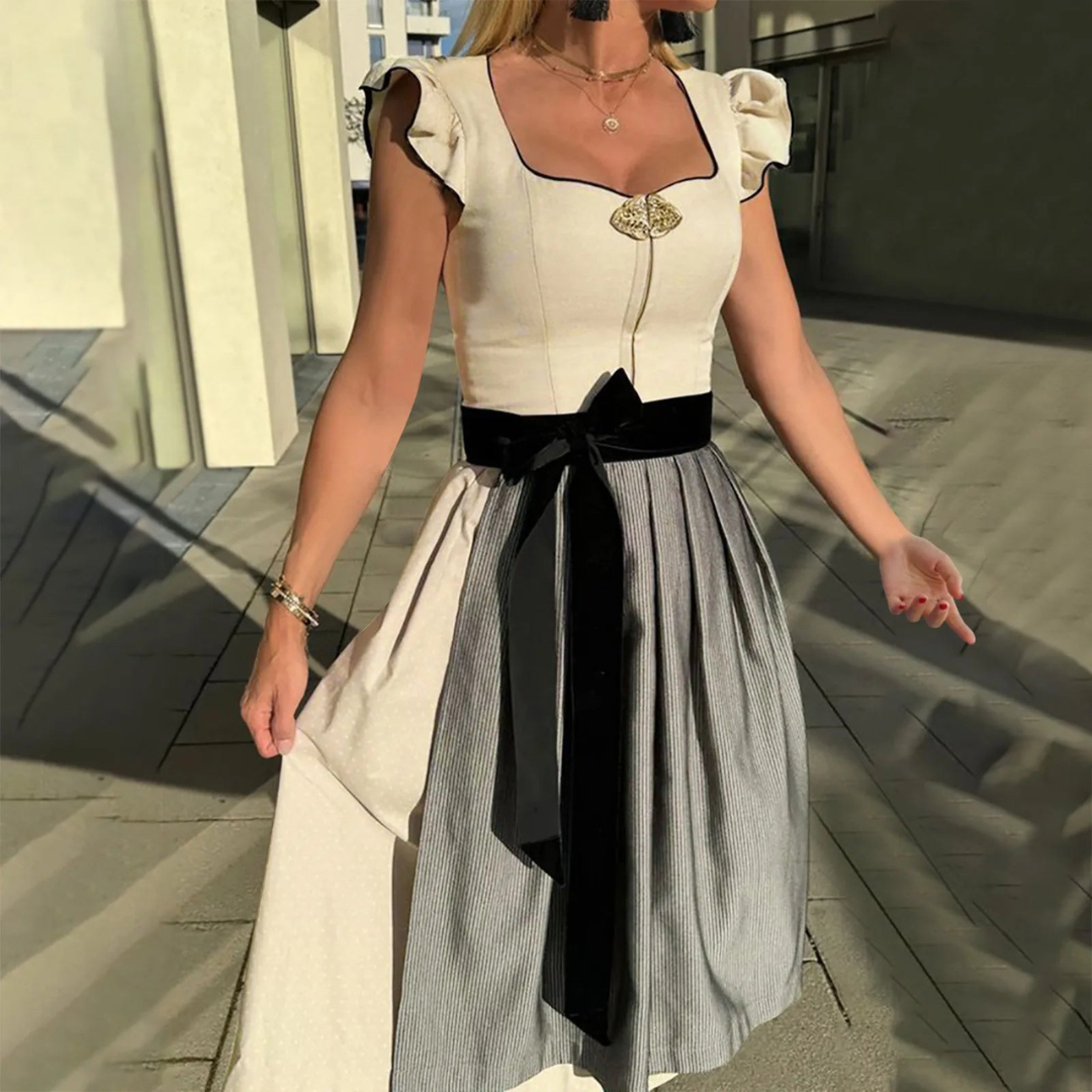 Frau in traditionellem Dirndl mit schwarzem Samtgürtel und Rüschenärmeln, steht im Sonnenlicht. Perfekt für Oktoberfest, Trachtenmode, bayerische Kleidung.