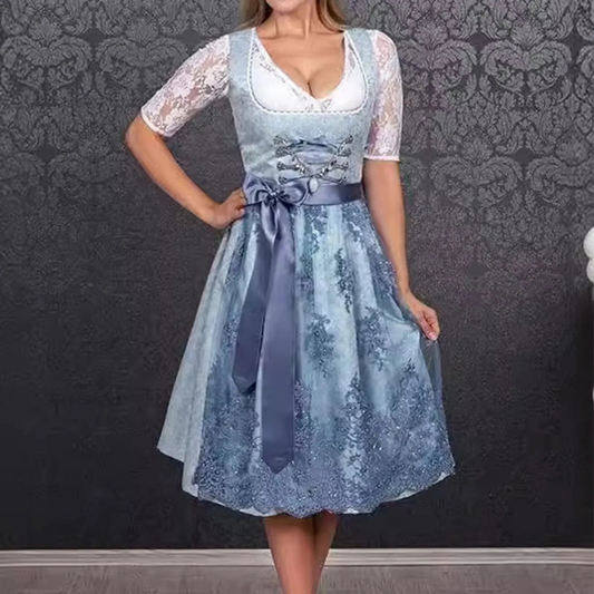 Frau in traditionellem blauen Dirndl mit Spitzenärmeln vor gemusterter Tapete. Oktoberfest Mode, bayerische Tracht, elegante Damenbekleidung.