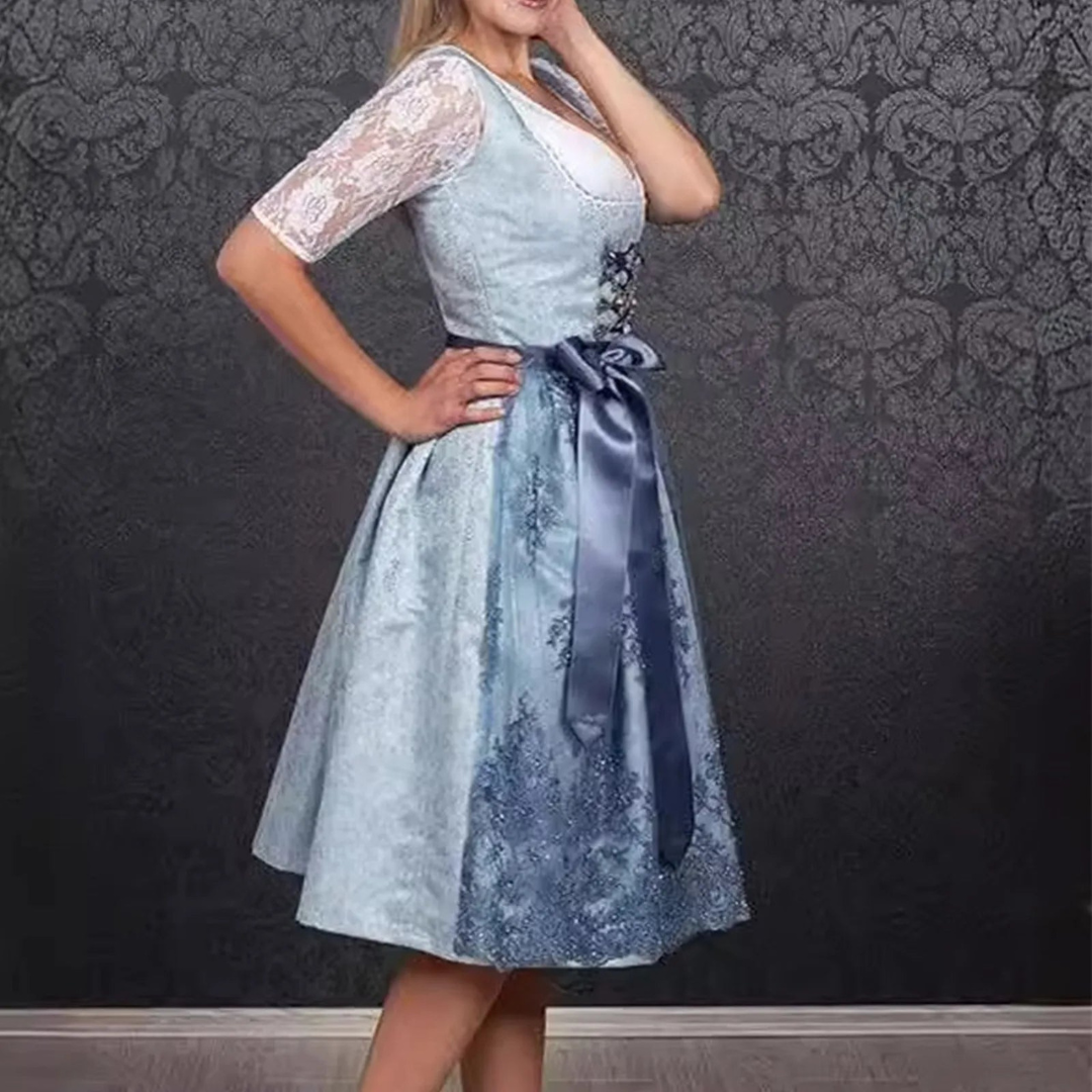 Frau in traditionellem blauen Dirndl mit Spitzenärmeln und Schleife, vor dunklem, gemustertem Hintergrund. Oktoberfest, Trachtenmode, bayerische Kleidung.