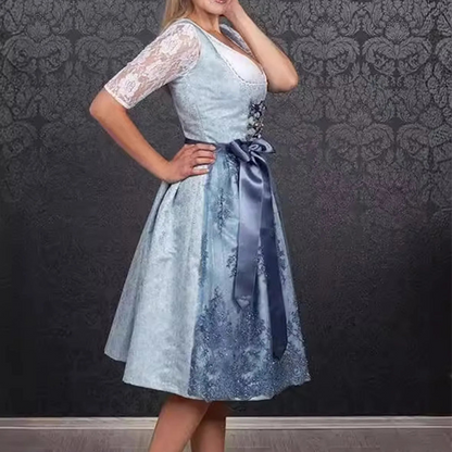 Frau in traditionellem blauen Dirndl mit Spitzenärmeln und Schleife, vor dunklem, gemustertem Hintergrund. Oktoberfest, Trachtenmode, bayerische Kleidung.