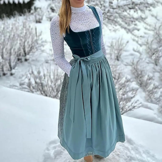 Frau in traditionellem blauen Dirndl mit weißer Spitzenbluse im verschneiten Garten. Traditionelle Tracht, Wintermode, bayerische Kleidung.