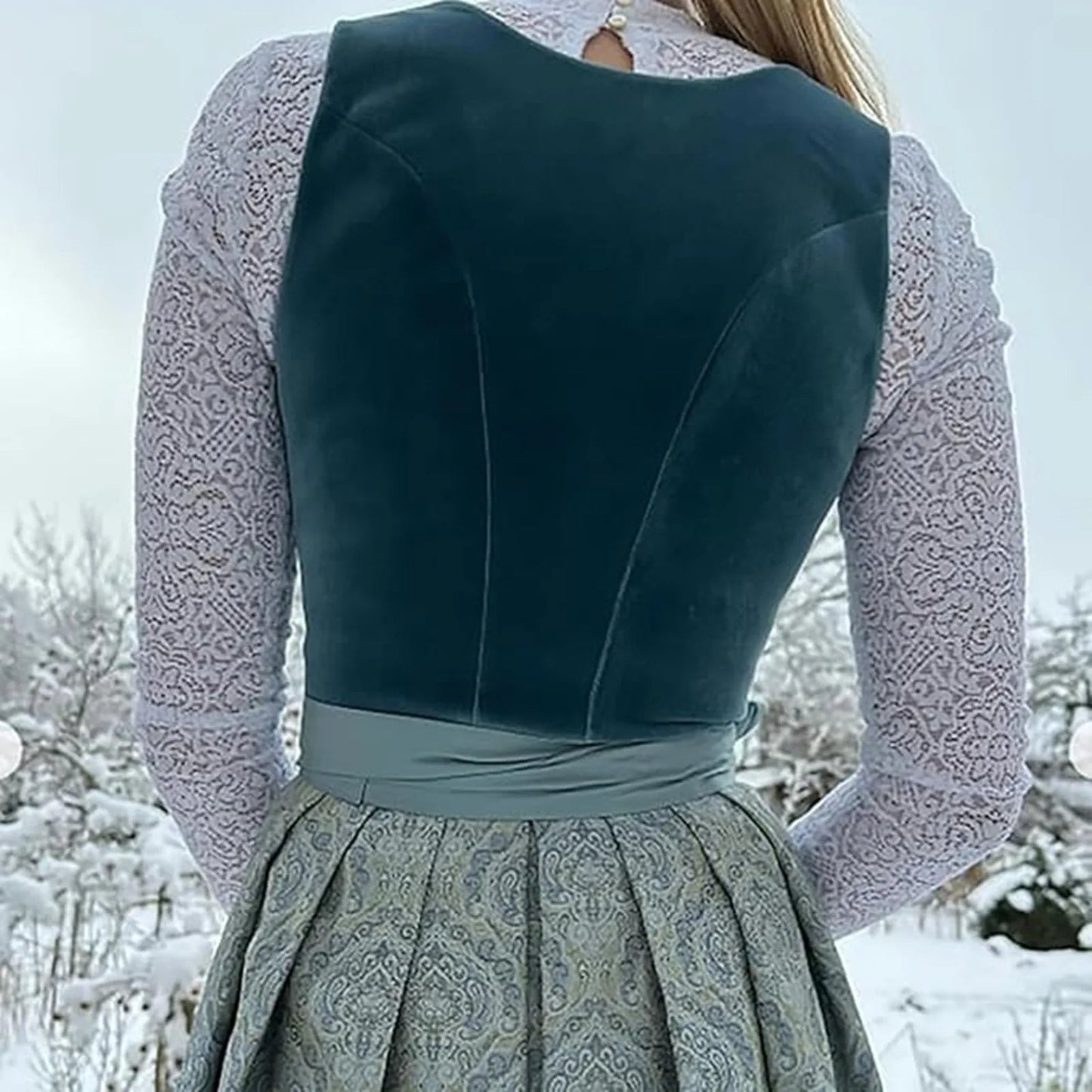 Frau in traditioneller Tracht mit blauem Samtmieder und grauem Rock, im verschneiten Winterhintergrund. Traditionelle Mode, Winterlandschaft.
