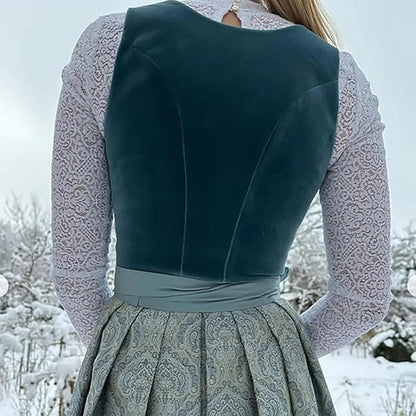 Frau in traditioneller Tracht mit blauem Samtmieder und grauem Rock, im verschneiten Winterhintergrund. Traditionelle Mode, Winterlandschaft.