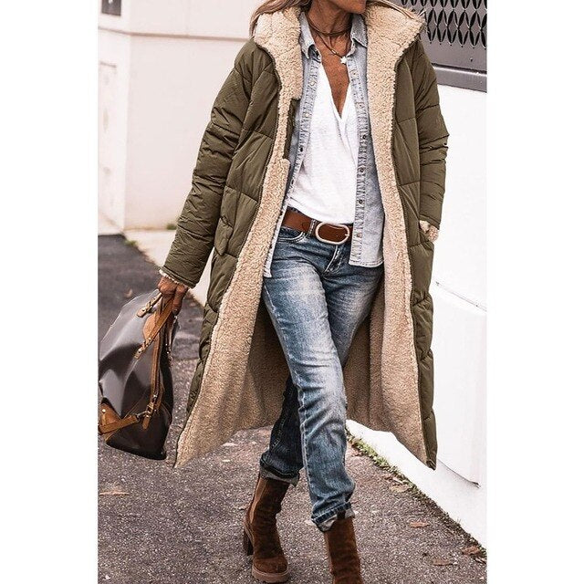 Frau in olivgrünem, langem Wintermantel mit Fellfutter, Jeans und braunen Stiefeln, trägt braune Tasche. Modischer Winterlook für Damen.