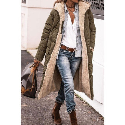 Frau in olivgrünem, langem Wintermantel mit Fellfutter, Jeans und braunen Stiefeln, trägt braune Tasche. Modischer Winterlook für Damen.