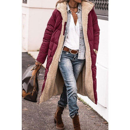 Frau in langem, weinrotem Wintermantel mit Fellfutter, Jeans und braunen Stiefeln, trägt braune Handtasche. Modischer Winterlook für Damen.