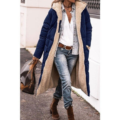 Frau in blauem, langem Wintermantel mit Fellfutter, Jeans und braunen Stiefeln, trägt braune Handtasche. Modischer Winterlook, Straßenstil.
