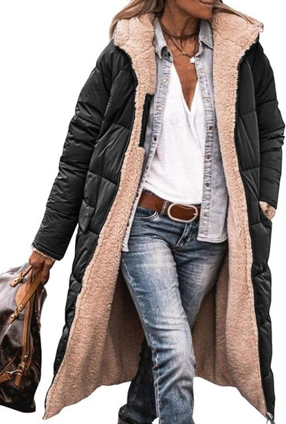 Frau in schwarzem, langem Steppmantel mit beigem Futter, weißem T-Shirt, Jeans und braunem Gürtel, hält braune Tasche. Wintermode, Damenbekleidung.