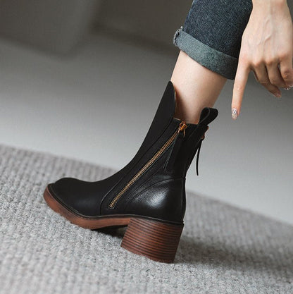 Schwarze Lederstiefelette mit Blockabsatz und seitlichem Reißverschluss, getragen von einer Person auf grauem Teppich. Modische Damenstiefel.