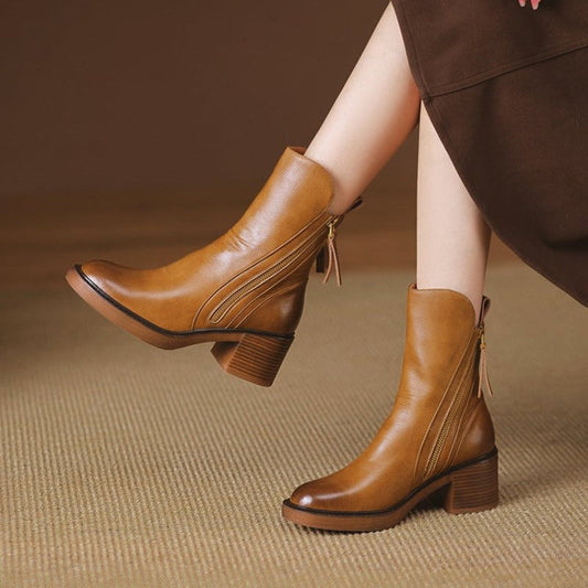 Braune Damenstiefeletten aus Leder mit Blockabsatz und Reißverschluss, stilvoll kombiniert mit einem braunen Rock, auf beigem Teppich.