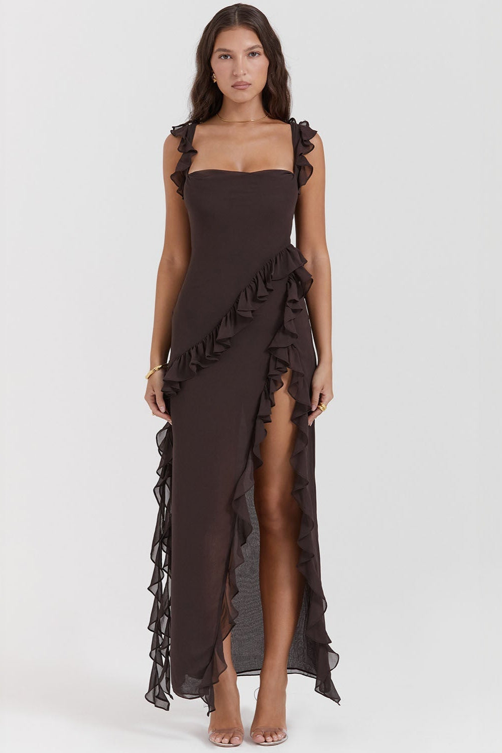 Frau in elegantem, schwarzem Abendkleid mit Rüschen und hohem Schlitz, stehend vor weißem Hintergrund. Mode, Abendgarderobe, Damenkleidung.