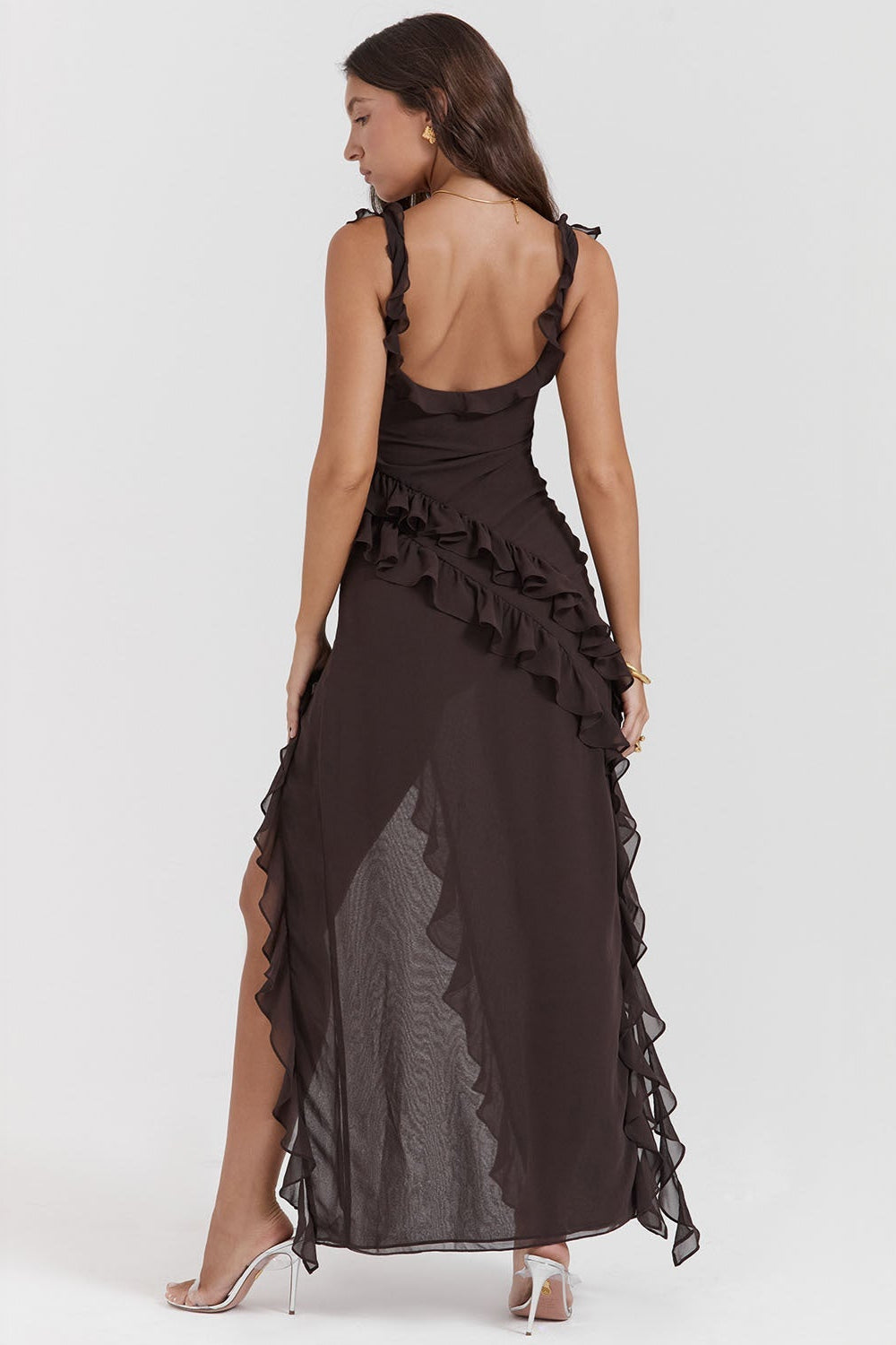 Frau in elegantem, schwarzem Rüschenkleid mit asymmetrischem Schnitt und transparentem Saum, trägt weiße High Heels. Perfekt für Abendmode.
