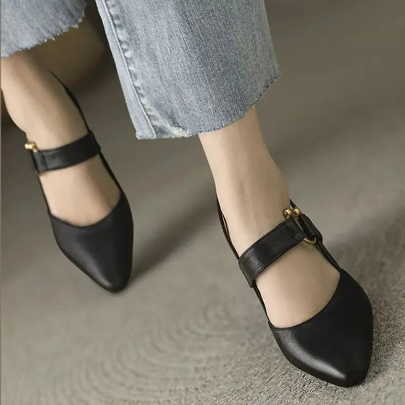 Damenfüße in schwarzen Mary Jane Schuhen mit goldenen Schnallen, kombiniert mit hellblauen Jeans. Modetrend, elegante Damenschuhe, Freizeitlook.