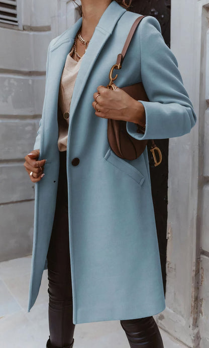 Frau in hellblauem Mantel, beige Bluse und schwarzer Hose, hält braune Handtasche. Modischer Herbstlook, eleganter Damenmantel, Streetstyle.