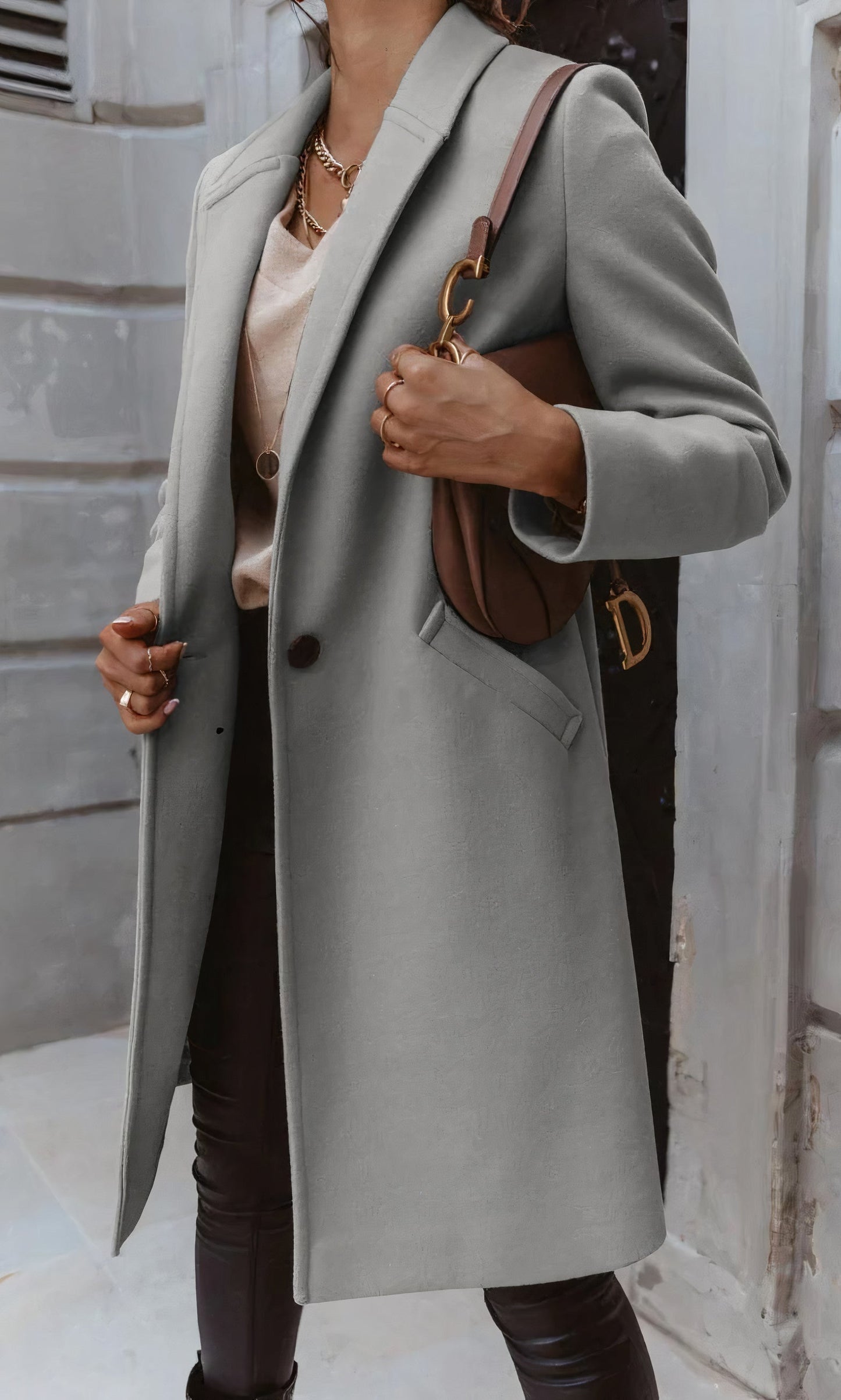 Frau in grauem Mantel, brauner Lederhandtasche, beiger Bluse und schwarzer Hose vor urbanem Hintergrund. Elegante Herbstmode, Streetstyle.