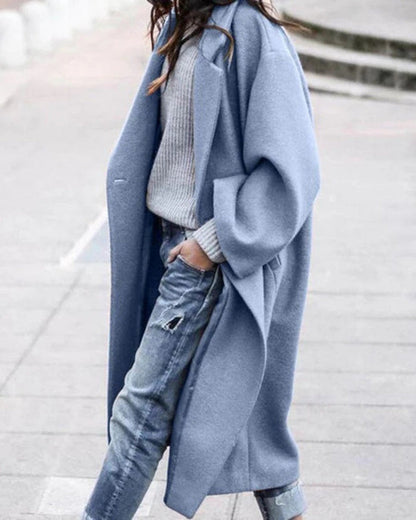 Frau in blauem Wollmantel, grauem Pullover und zerrissenen Jeans spaziert auf Gehweg. Modetrend, Herbstmode, lässiger Streetstyle.