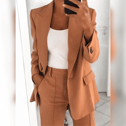 Dame in elegantem, braunem Anzug mit weißem Top, hält Smartphone. Businessmode, stilvoller Look, moderne Damenbekleidung, Büro-Outfit.