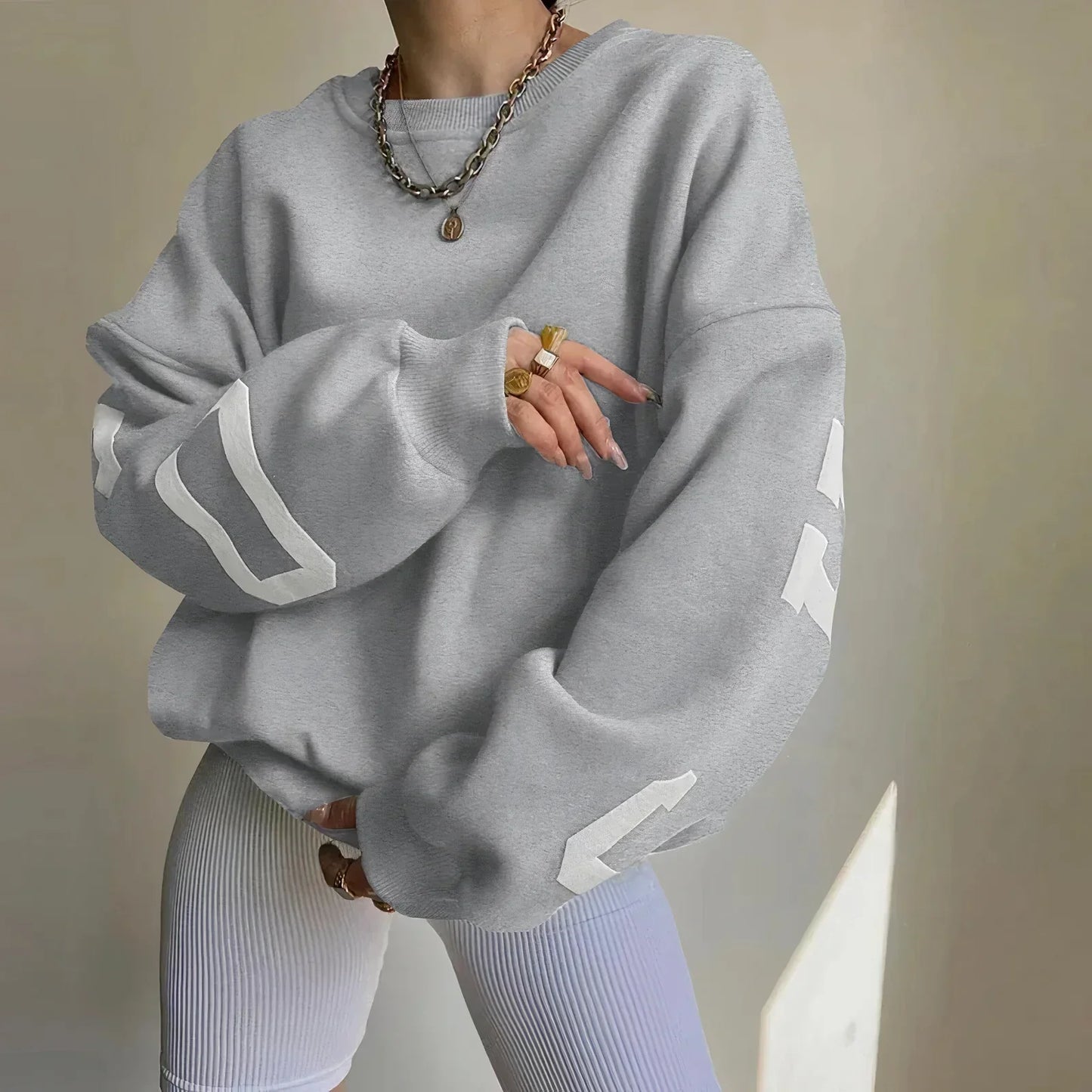 Grauer Oversize-Pullover mit weißen Streifen, kombiniert mit weißen gerippten Leggings. Modischer Look, ideal für lässige Outfits und Streetwear.