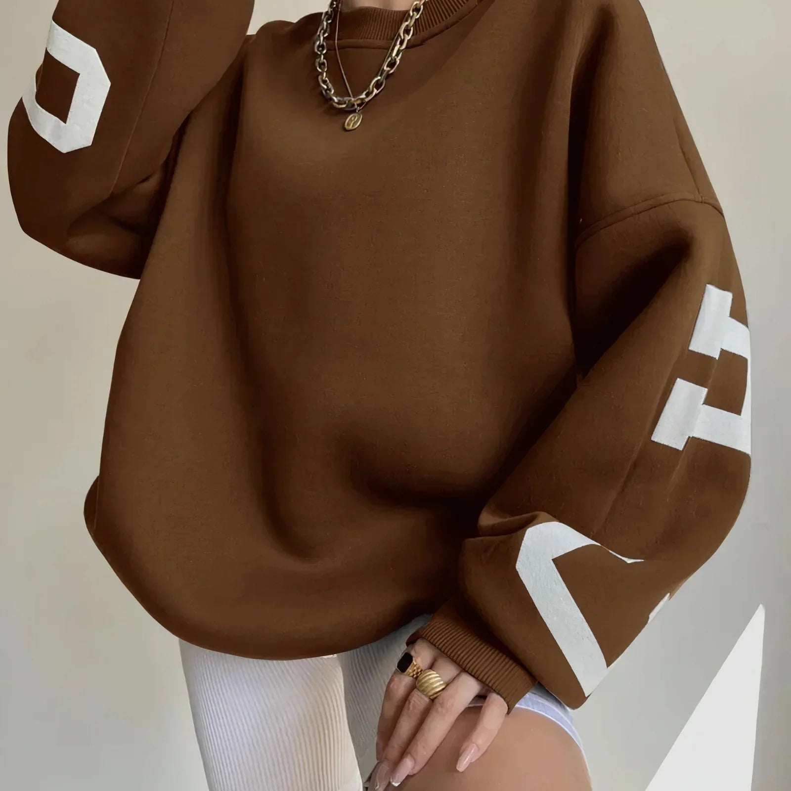 Brauner Oversize-Pullover mit weißen Buchstaben auf den Ärmeln, kombiniert mit weißen Radlerhosen. Modetrend, lässiger Stil, Damenbekleidung.
