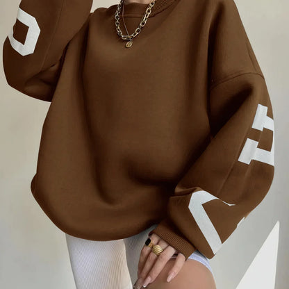 Brauner Oversize-Pullover mit weißen Buchstaben auf den Ärmeln, kombiniert mit weißen Radlerhosen. Modetrend, lässiger Stil, Damenbekleidung.