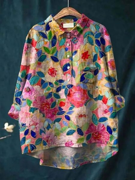 Bunte Damenbluse mit floralem Muster, hängend auf einem Holzkleiderbügel. Lebendige Farben und Blumenmuster, ideal für Frühling und Sommermode.