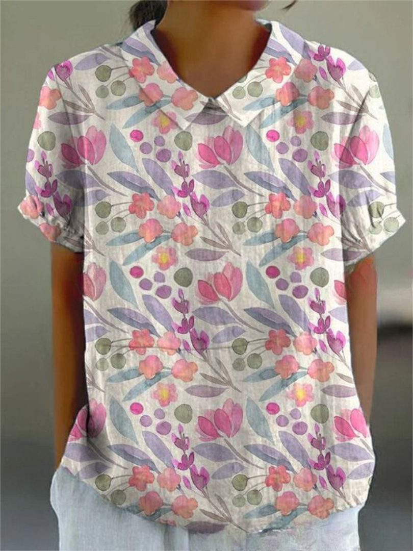 Frau trägt kurzärmlige Bluse mit buntem Blumenmuster, rosa und lila Blüten, grünen Blättern. Modische Damenbekleidung, sommerlicher Look.