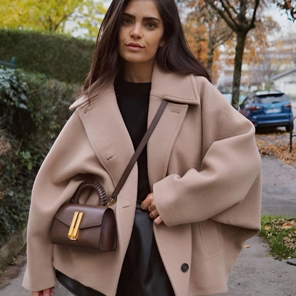 Frau in beigem Mantel mit brauner Handtasche spaziert im Herbst. Modetrend, Damenmode, Herbstoutfit, stilvolle Kleidung, Straßenmode.