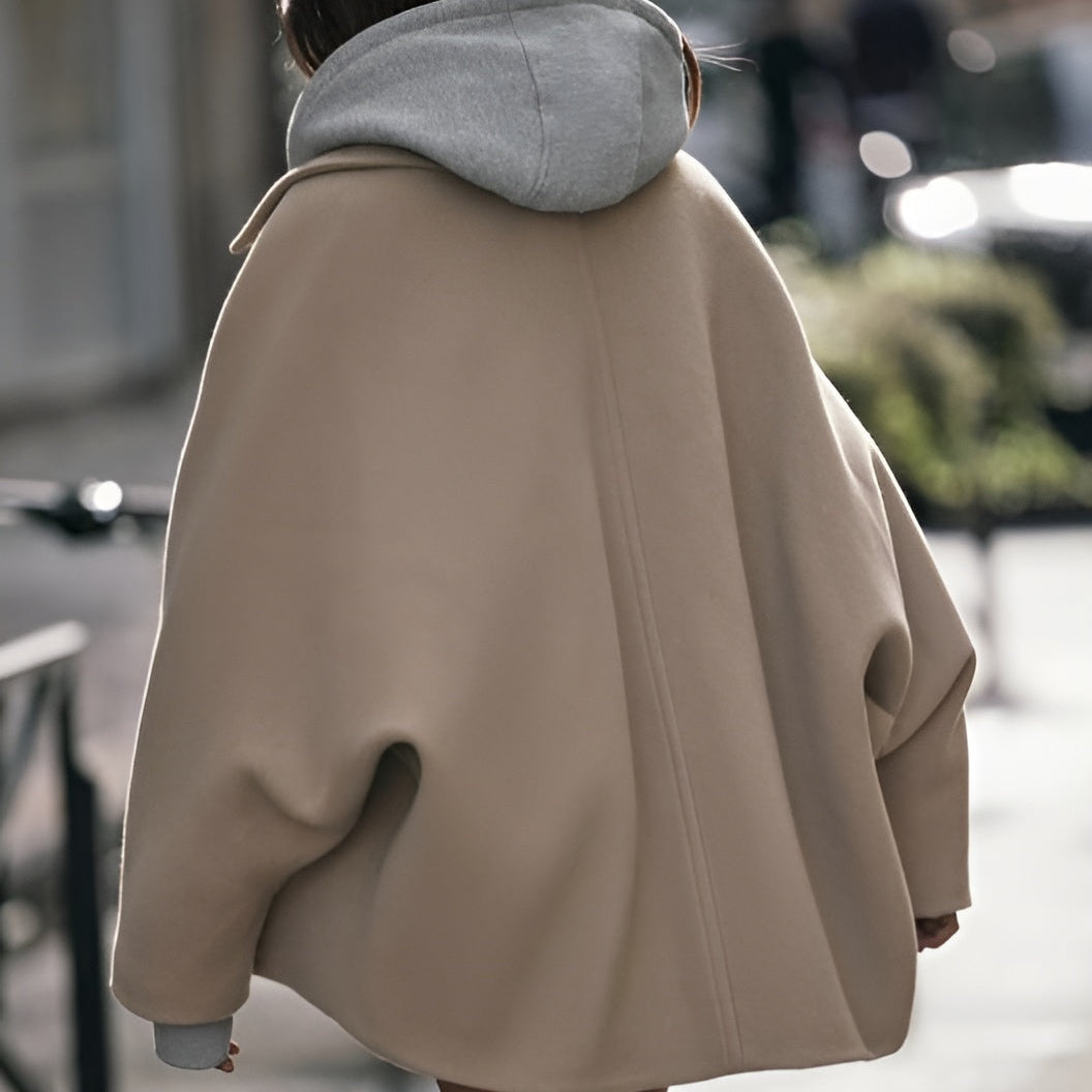Frau in beigem Oversize-Mantel und grauem Kapuzenpullover auf Straße. Modetrend, Herbstmode, Streetstyle, lässiger Look.