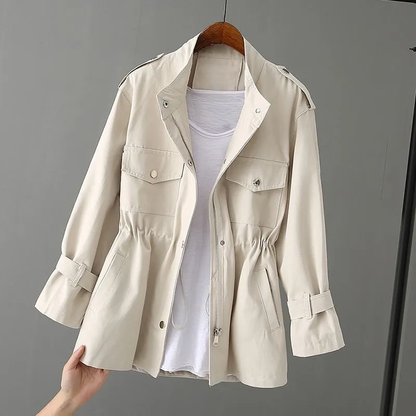 Beige Damenjacke mit Kordelzug, Reißverschluss und Taschen, über weißem T-Shirt auf Holzkleiderbügel. Modische Übergangsjacke für Frühling.