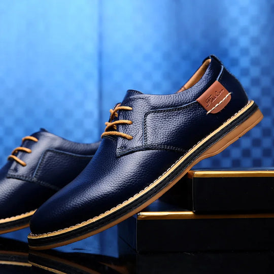 Elegante blaue Lederschuhe für Herren mit braunen Schnürsenkeln, auf schwarzem und goldenem Podest. Perfekt für formelle Anlässe und Business-Outfits.