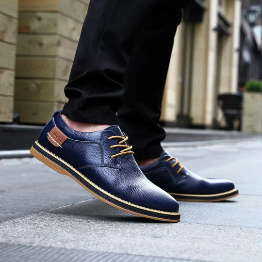 Elegante blaue Lederschuhe für Herren mit braunen Schnürsenkeln, getragen auf einer städtischen Straße. Ideal für Business- und Freizeitoutfits.