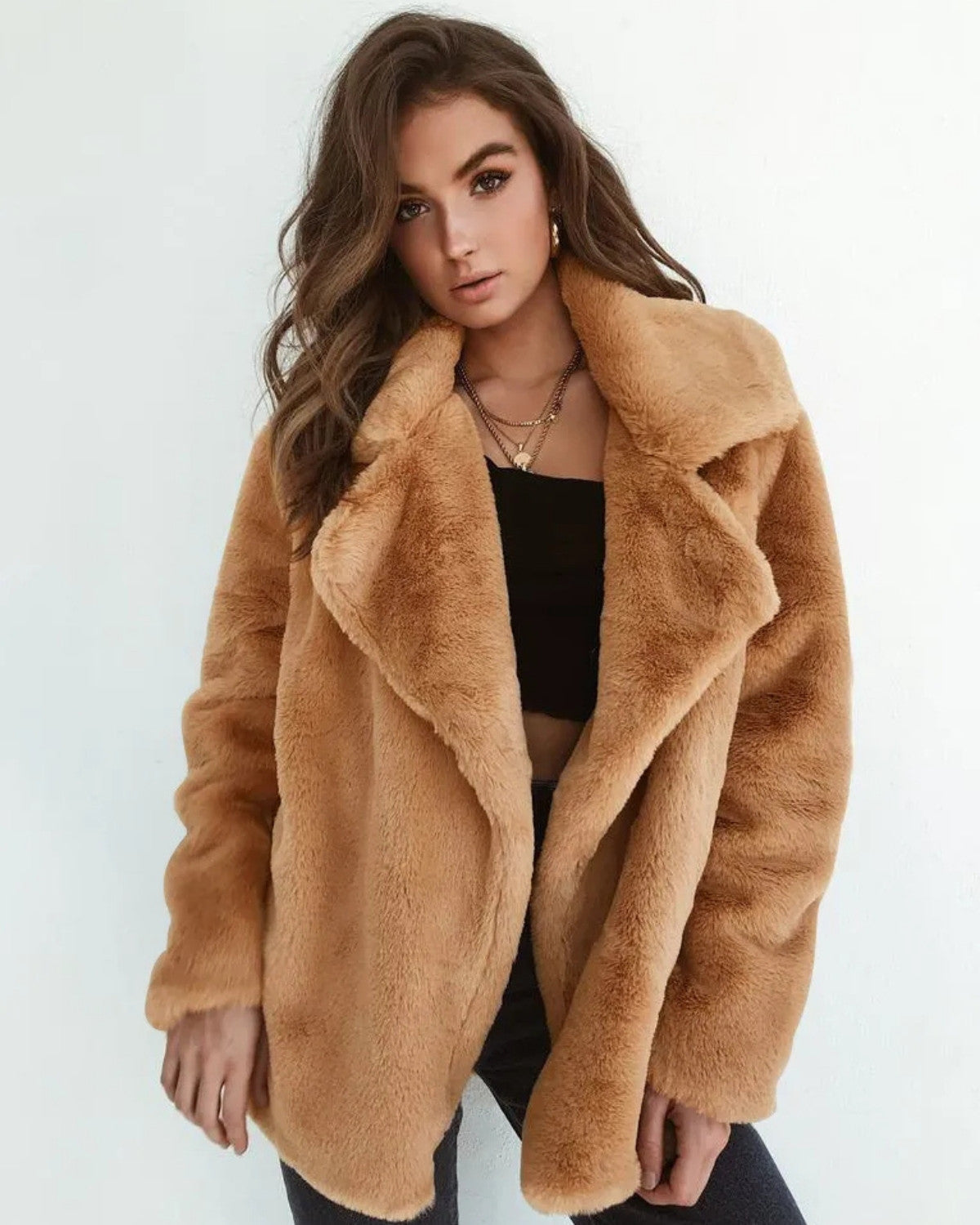 Frau in braunem Kunstpelzmantel, schwarzem Top und Jeans vor weißem Hintergrund. Modetrend, Wintermode, stilvolle Damenbekleidung.