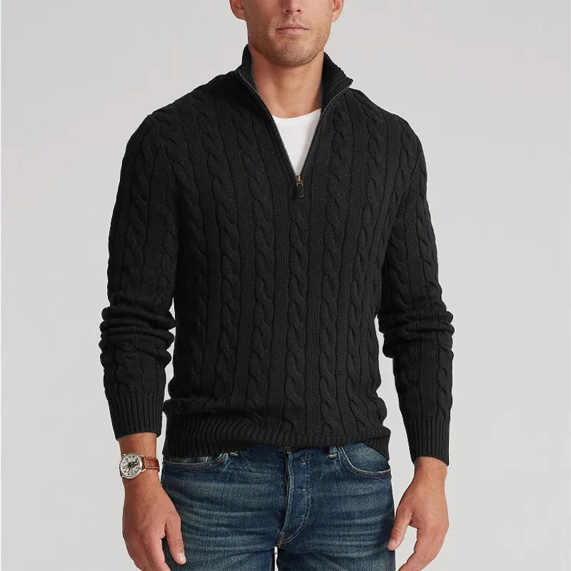 Mann trägt schwarzen Zopfmuster-Pullover mit Reißverschluss, kombiniert mit blauer Jeans. Modischer Herren-Look, ideal für Herbst und Winter.