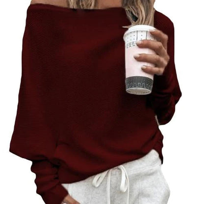 Frau in rotem Off-Shoulder-Pullover hält einen Kaffeebecher, trägt weiße Jogginghose. Modetrend, lässiger Stil, Herbstmode.