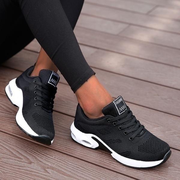 Schwarze Damen-Sneaker mit weißer Sohle auf Holzterrasse, modisches Design, atmungsaktives Material, ideal für Freizeit und Sport.