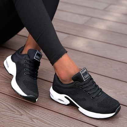 Schwarze Damen-Sneaker mit weißer Sohle auf Holzterrasse, modisches Design, atmungsaktives Material, ideal für Freizeit und Sport.