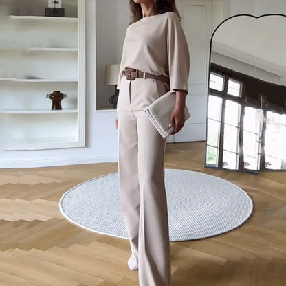 Frau in eleganter, beiger Hose und Oberteil, steht in modernem Wohnzimmer mit Parkettboden, rundem Teppich und großem Spiegel.