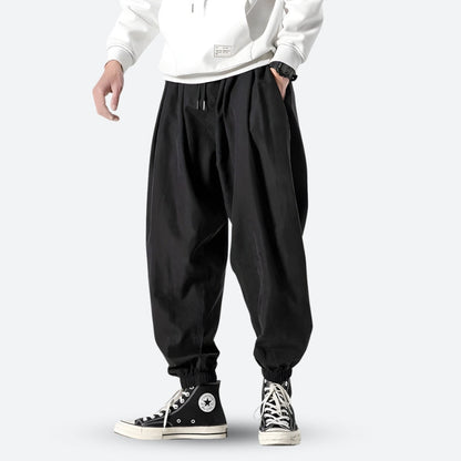 Mann in schwarzer Baggy-Hose und weißen Sneakers, lässiger Streetwear-Stil, modische Freizeitkleidung, urbaner Look.