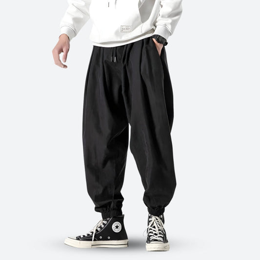 Mann in schwarzer Baggy-Hose und weißen Sneakers, lässiger Streetwear-Stil, modische Freizeitkleidung, urbaner Look.