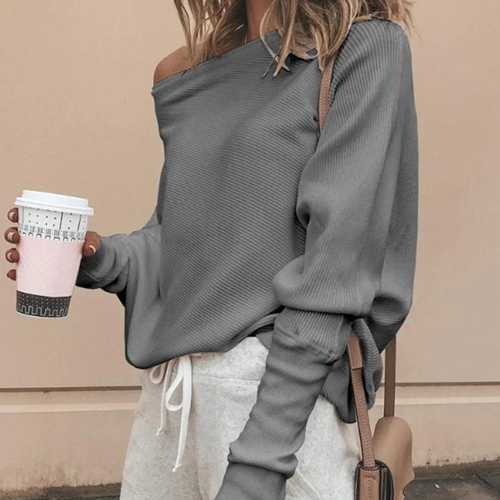 Frau in grauem Off-Shoulder-Pullover und Jogginghose hält Kaffeebecher. Modetrend, lässiger Stil, Herbstmode, Streetwear.
