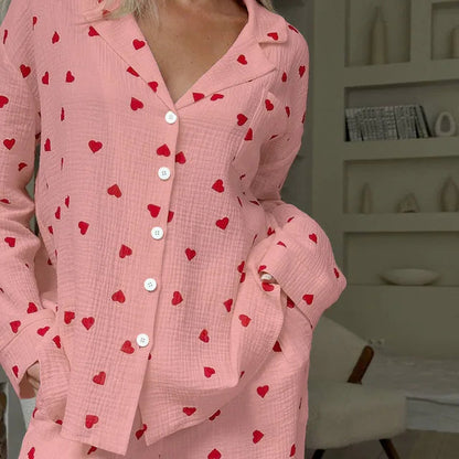Frau in rosa Pyjama mit roten Herzmustern, Knopfleiste und Kragen. Gemütliche Nachtwäsche, modernes Design, entspannte Atmosphäre im Hintergrund.