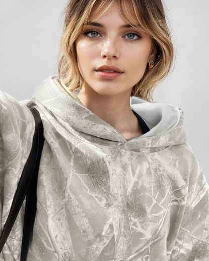 Junge Frau in grauem Camouflage-Hoodie, schaut direkt in die Kamera. Modetrend, lässiger Stil, urbaner Look, Herbstmode 2023.